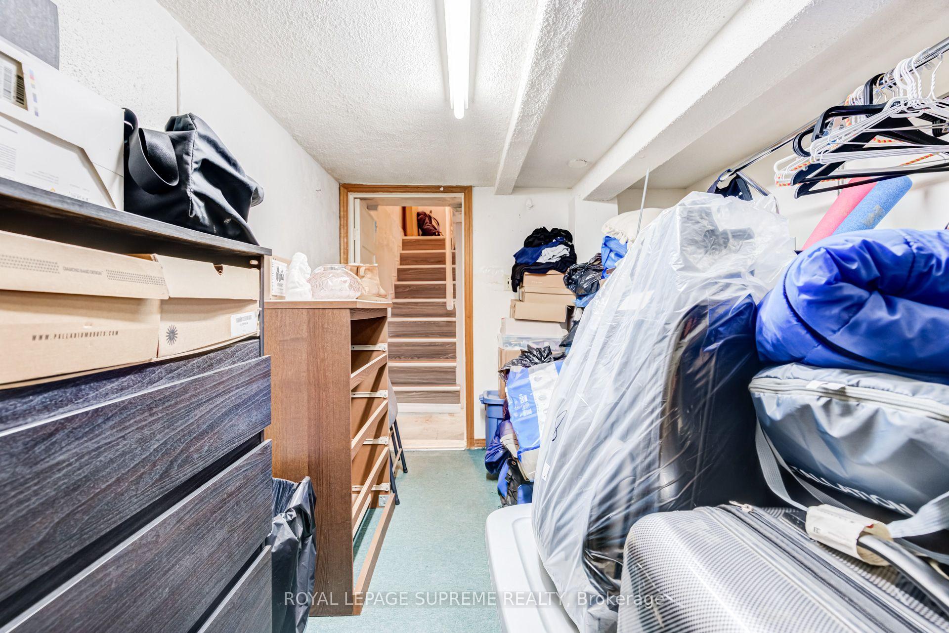 Storage room with shelves, boxes, hanging clothes, and stairs at the back.
