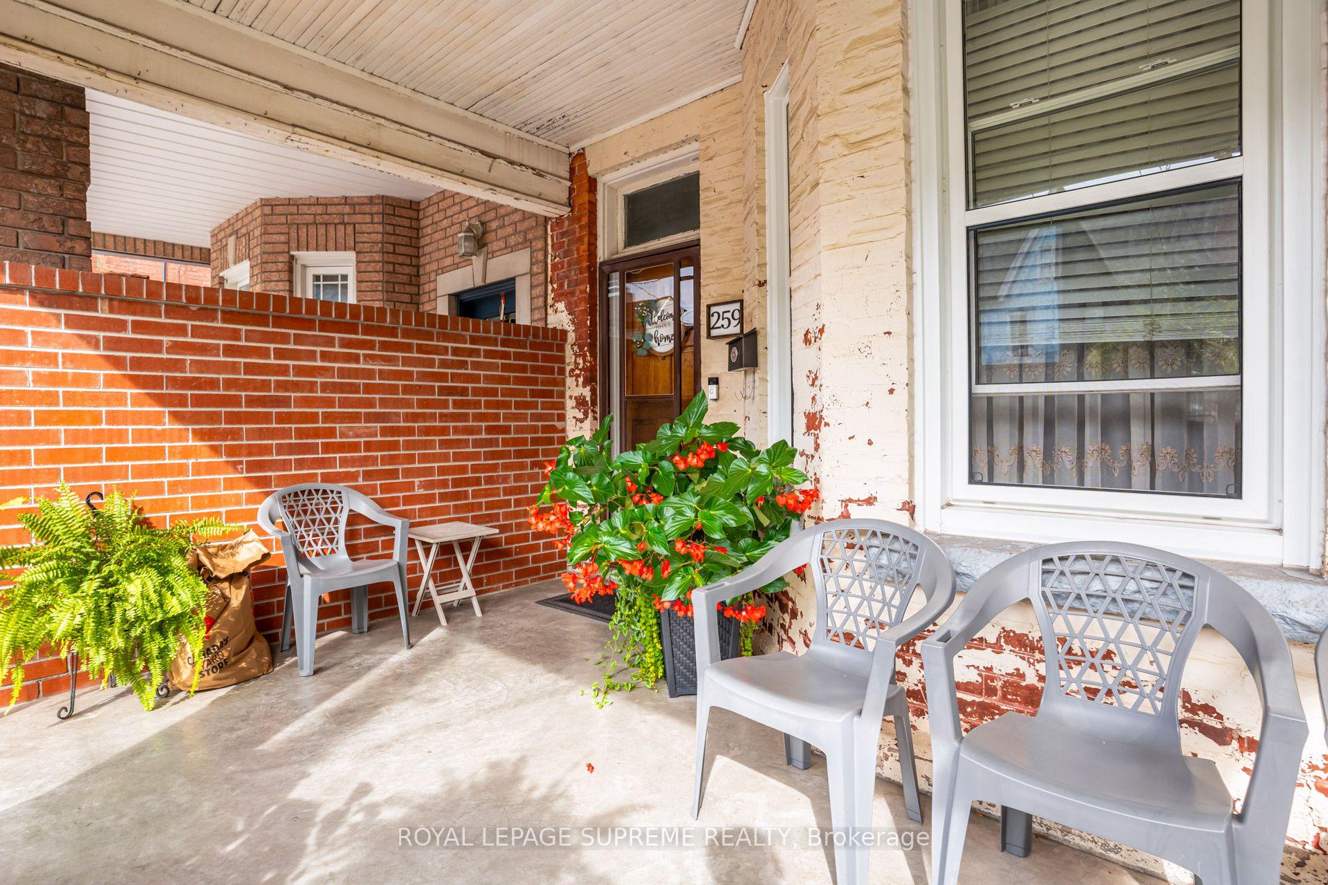 Covered brick porch with gray chairs, flowering plants, and a wooden front door.