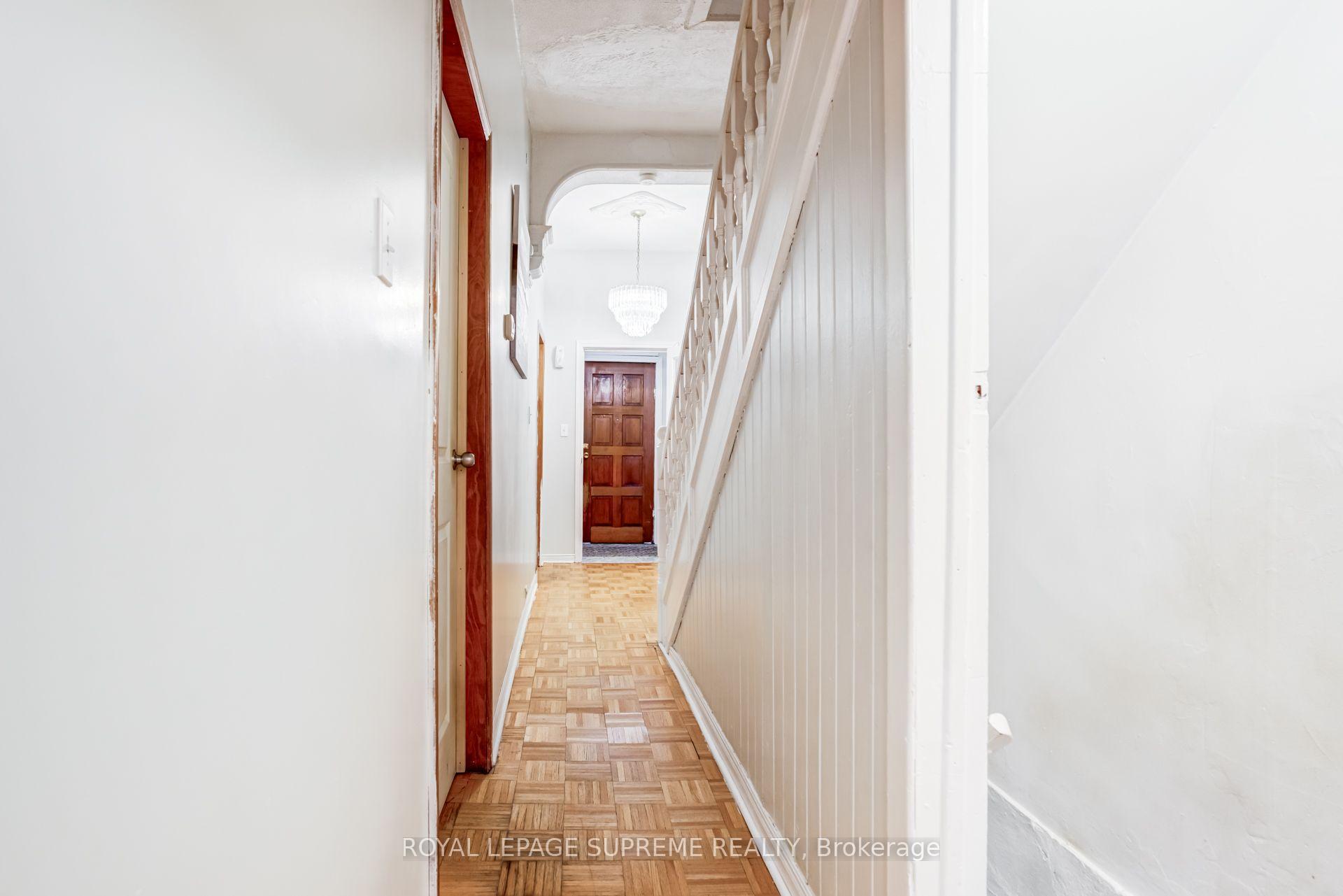 Hallway with parquet flooring, white staircase railing, and a dark wooden door beneath a crystal chandelier.