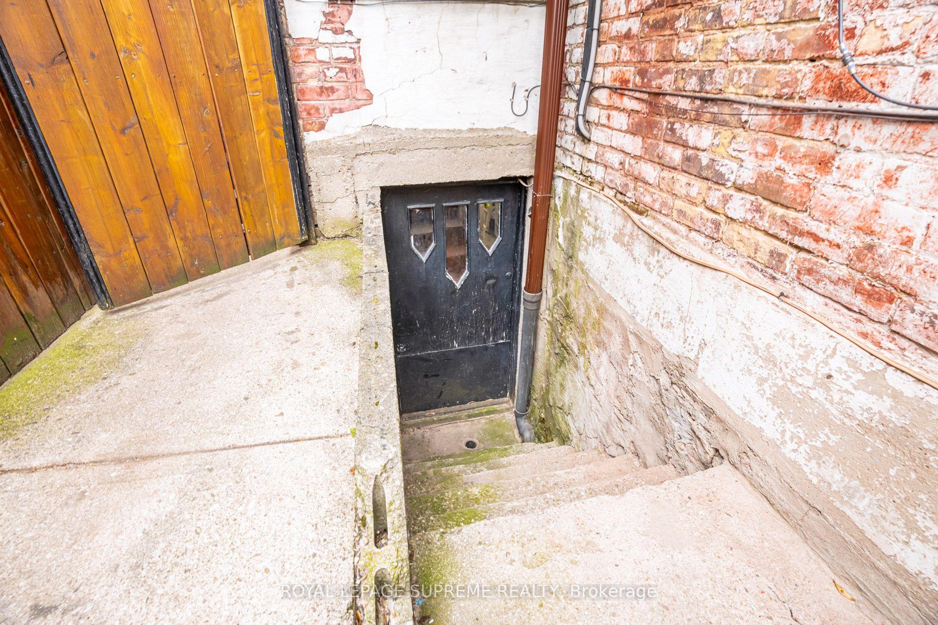 Below-grade entrance with concrete steps, a black door, weathered brick walls, and a wooden gate.