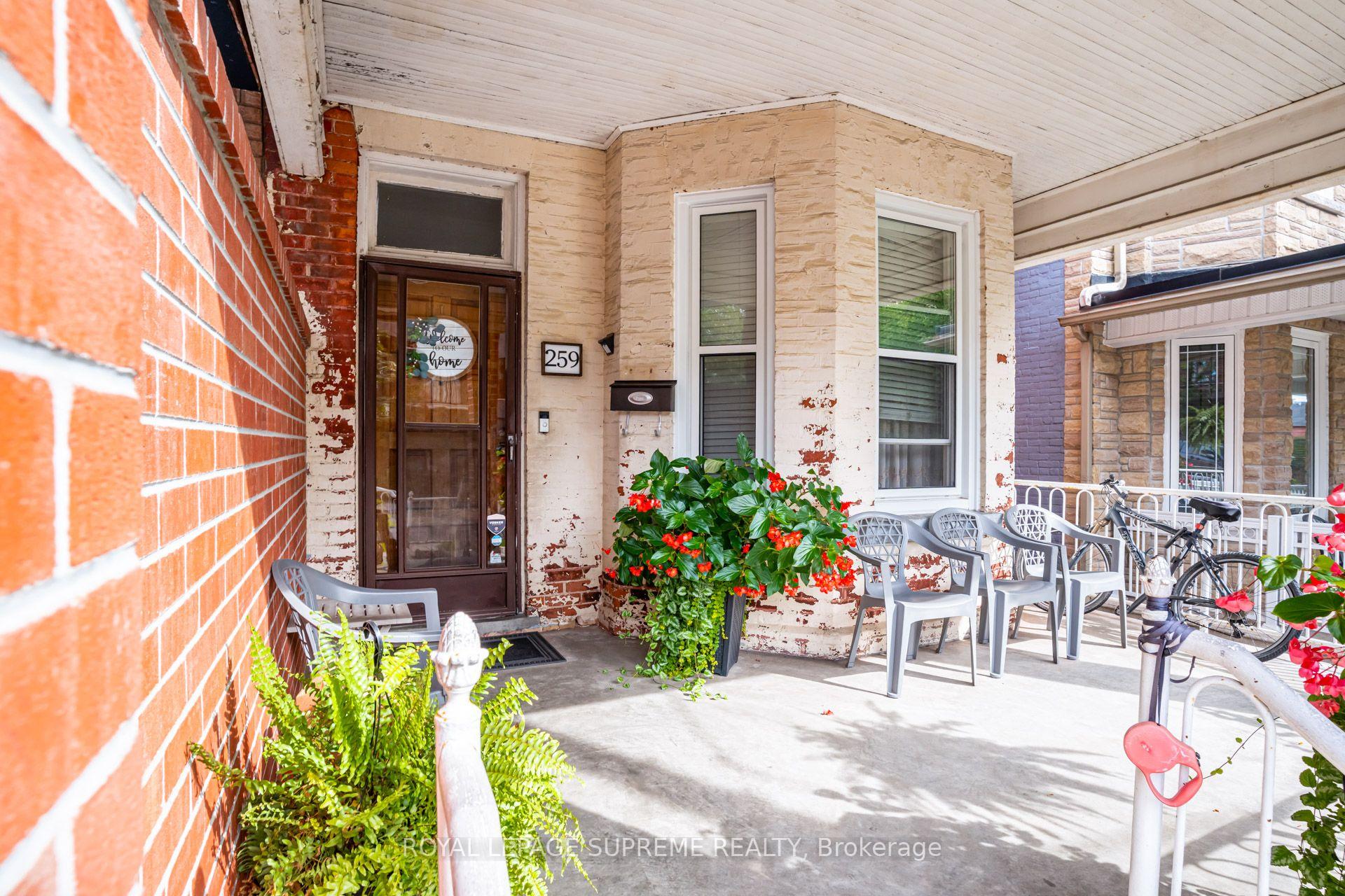 Front porch with a dark wood-and-glass entrance, gray chairs, bicycles, and flowering plants.