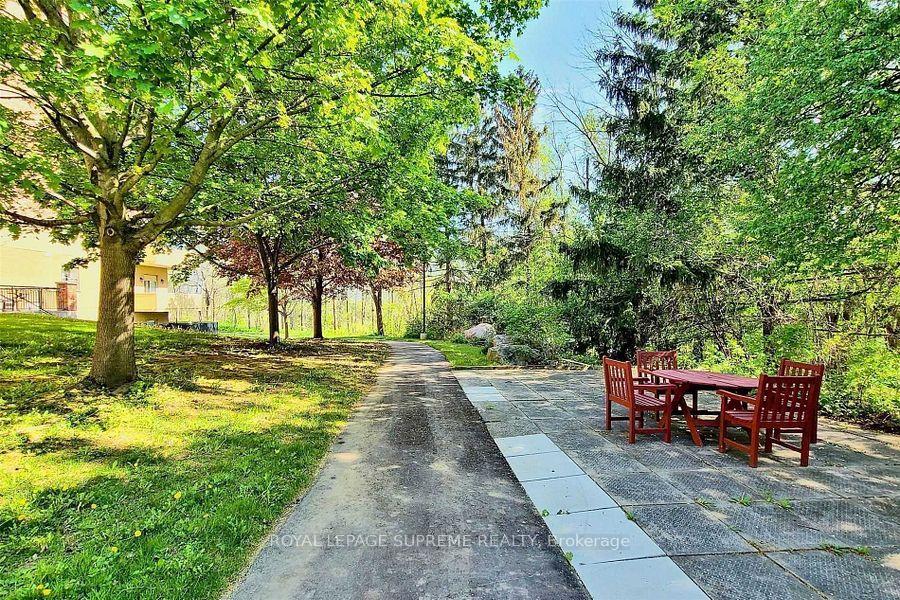 Landscaped courtyard with a tree-lined walkway and red wooden dining set on a stone patio.
