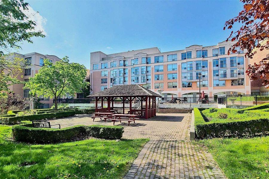 Condominium building behind a landscaped courtyard with a wooden picnic shelter and paved paths.