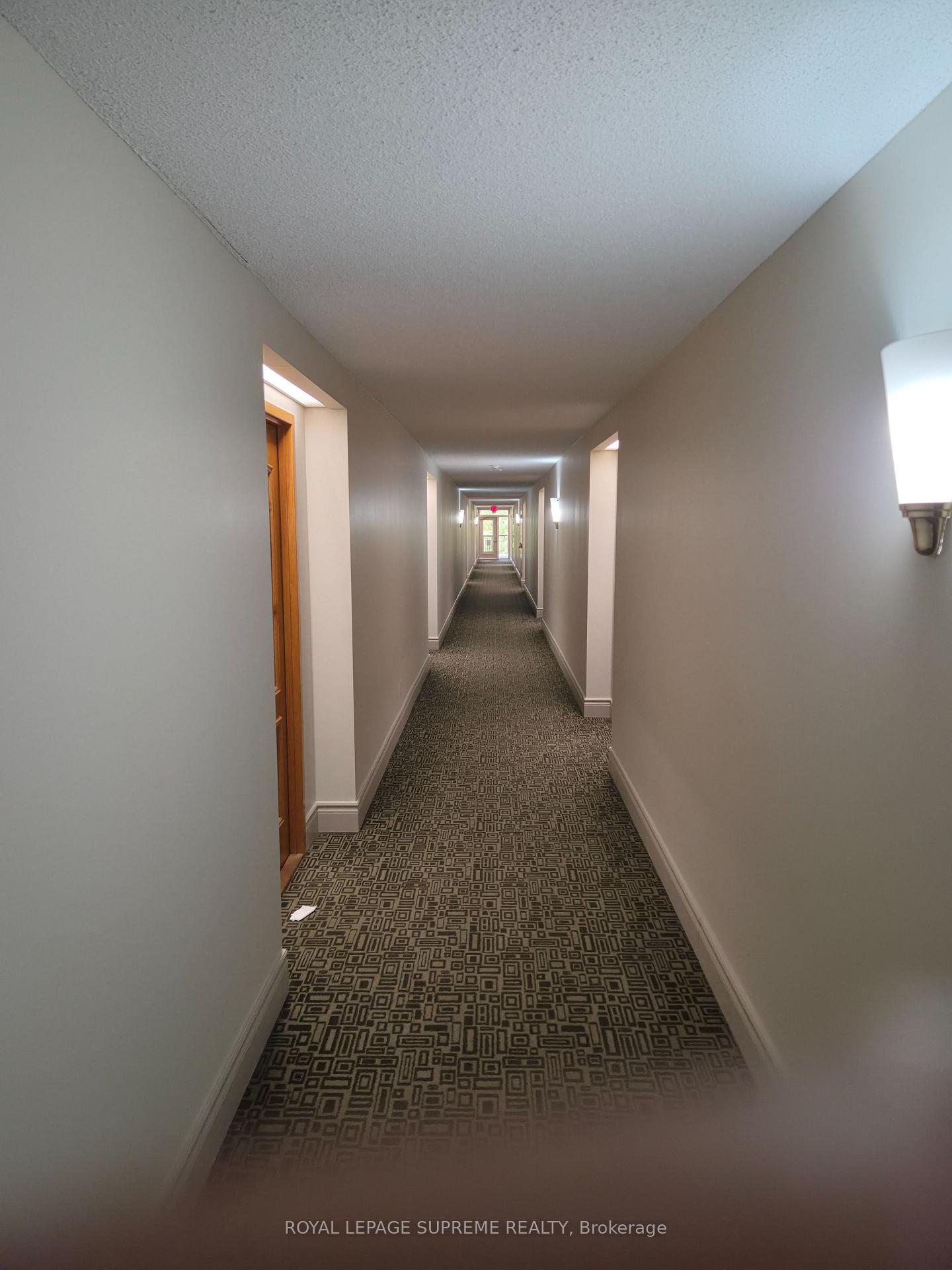 Residential building hallway with patterned carpet, wall sconces, and wooden apartment doors.