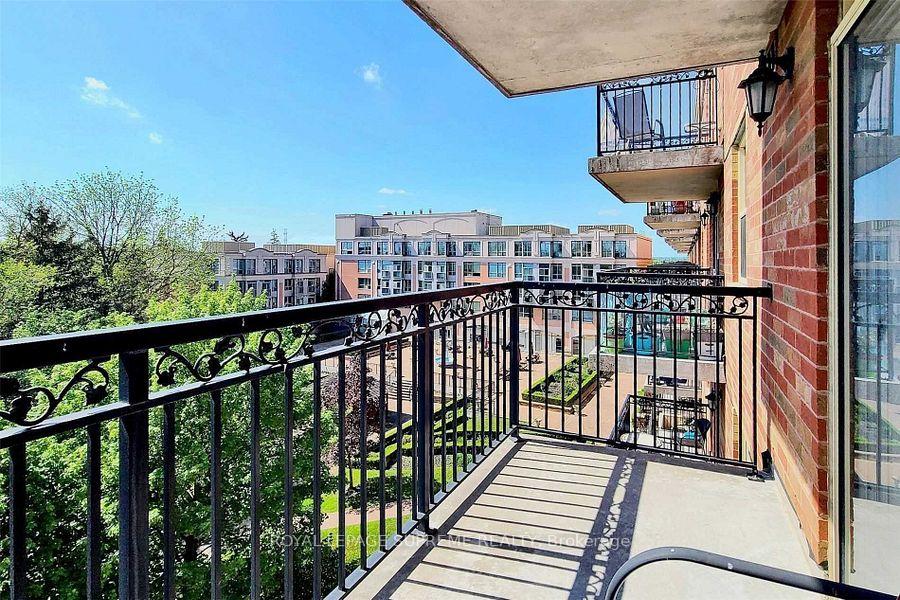 Covered condo balcony with ornate black railings overlooking trees and neighboring buildings.
