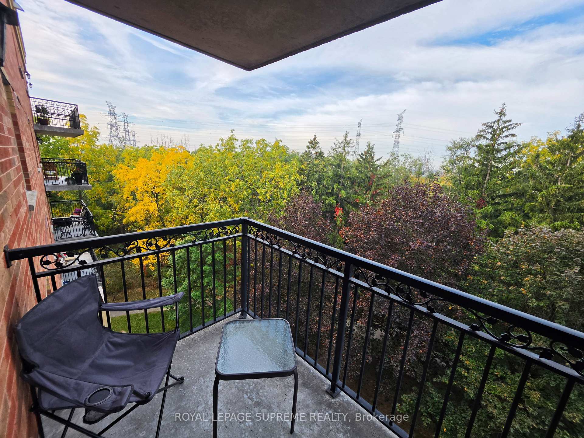 Apartment balcony overlooking autumn trees, with ornate black railings and a glass-top table.
