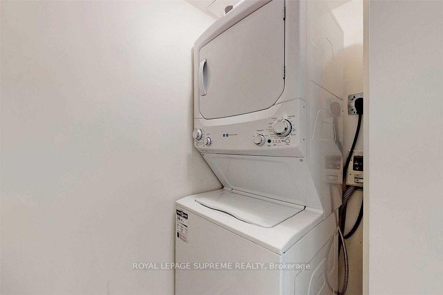 Stacked white washer and dryer in a narrow laundry closet, with hoses and hookups visible.