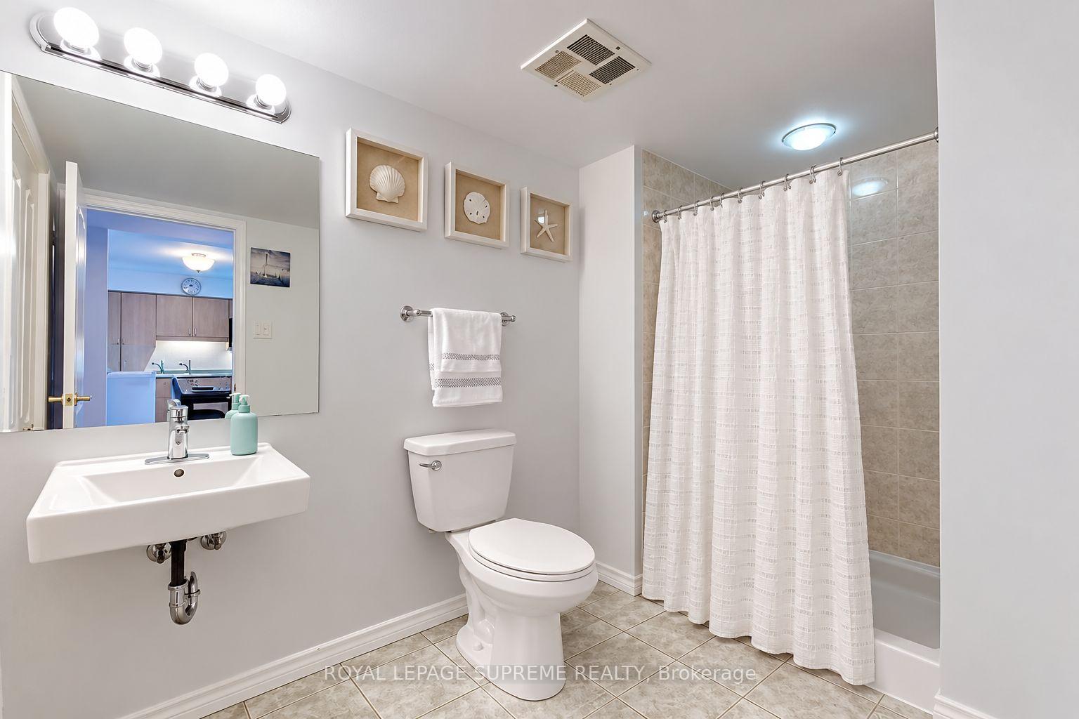 Bathroom with a wall-mounted sink, large mirror, toilet, and curtained tub with beige tile.