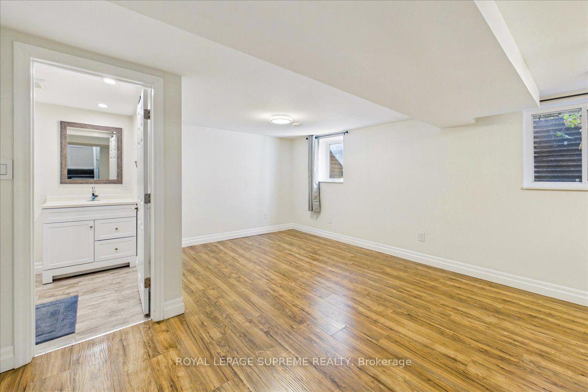 Vacant basement room with wood-look flooring and an adjoining bathroom vanity.