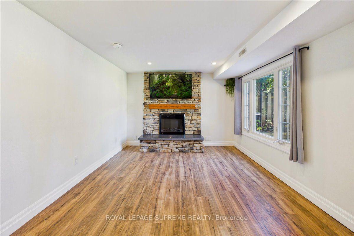 Empty living room with wood-look floors, a stone fireplace, and large curtained windows.