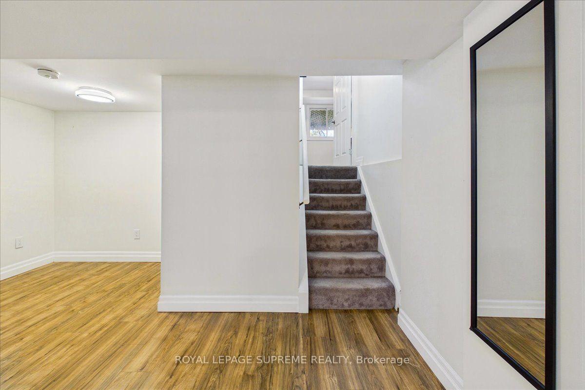 Lower-level room with wood-look flooring, carpeted stairs, and a tall black-framed mirror.