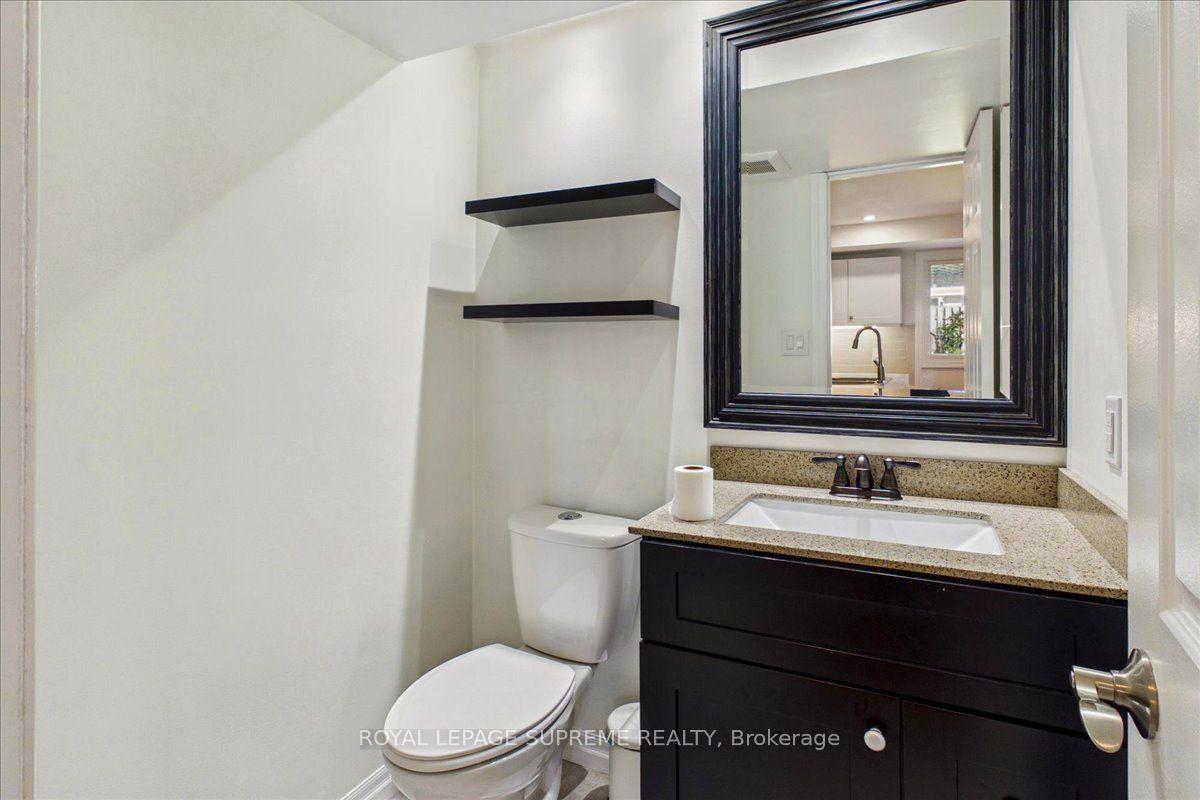 Bathroom with a dark vanity, speckled countertop, large black-framed mirror, and floating shelves above the toilet.