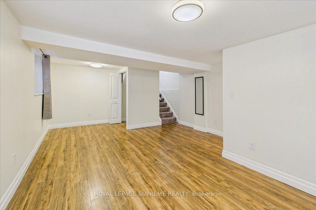 Empty lower-level room with wood-look flooring and stairs leading upstairs.