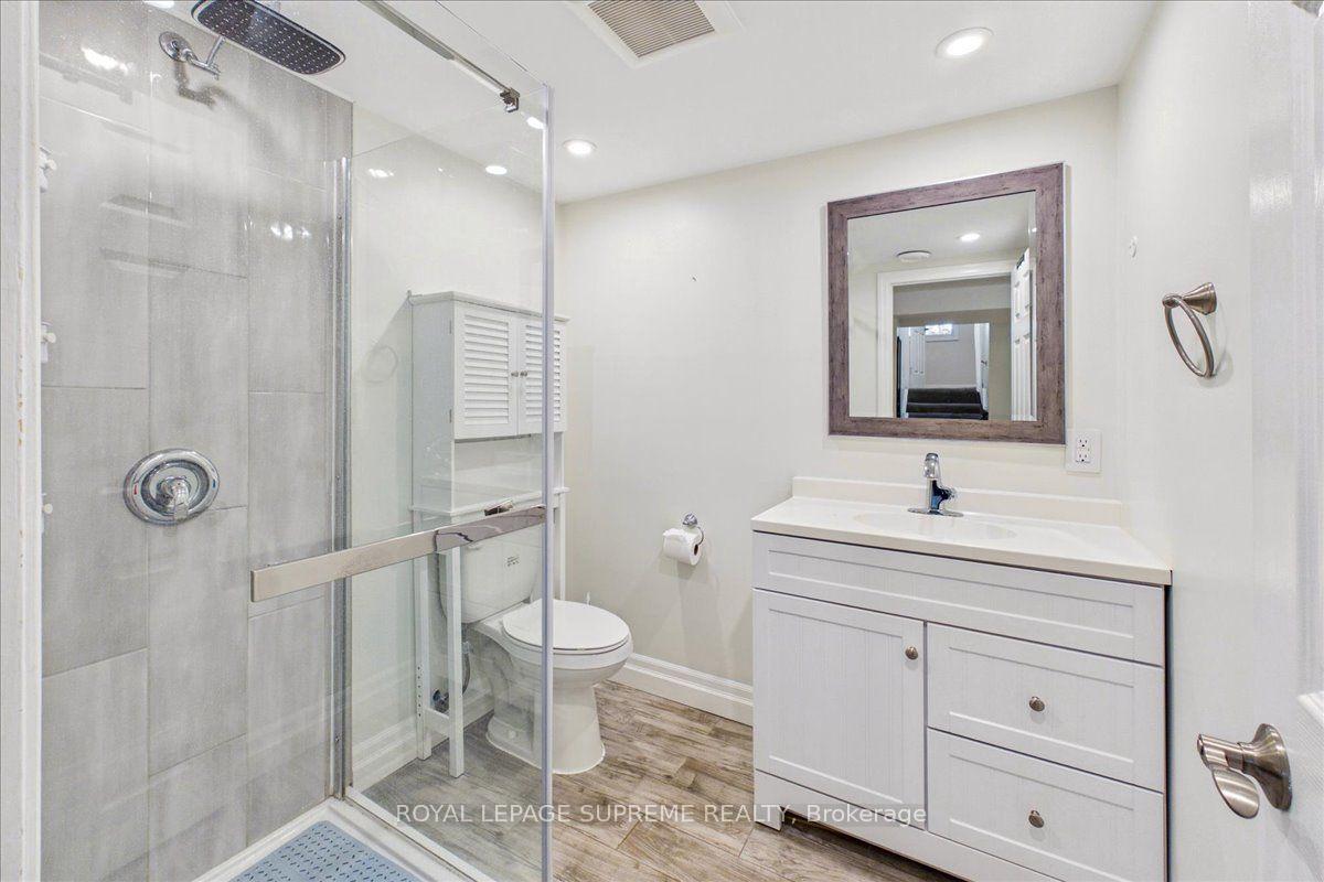 Lower-level bathroom with glass shower, white vanity, framed mirror, and wood-look floor.