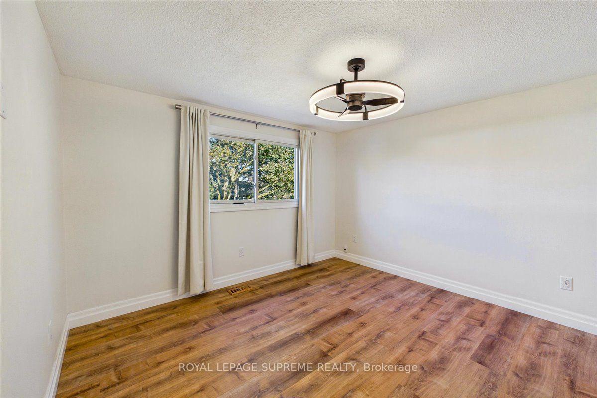 Empty bedroom with warm wood flooring, a curtained window, and a modern ceiling fan light.