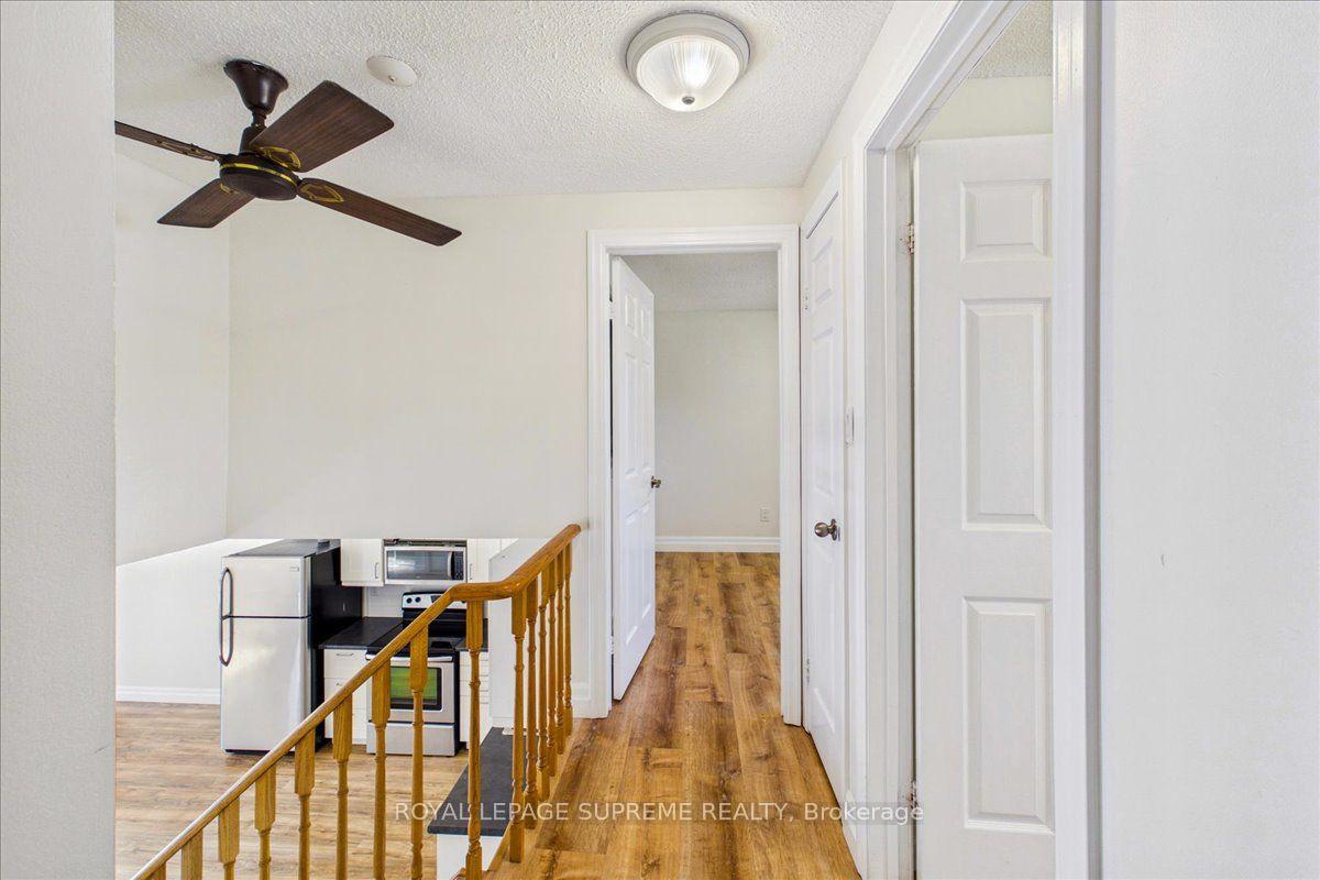 Upper-unit hallway with wood-look flooring, white paneled doors, and a compact kitchen beside the stair railing.
