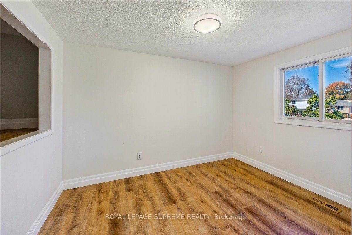 Empty room with wood-look flooring, white walls, and a window overlooking autumn trees.