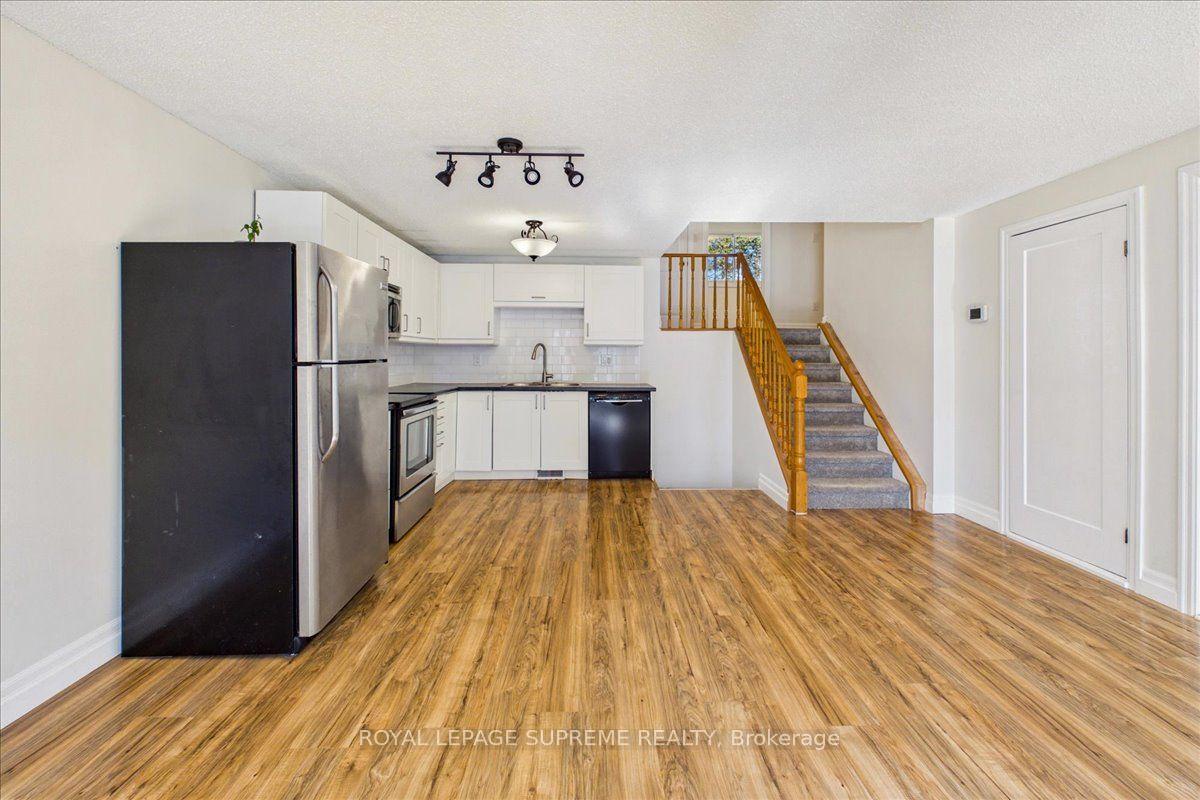 Unfurnished kitchen with white cabinets and stainless steel appliances beside a carpeted staircase.
