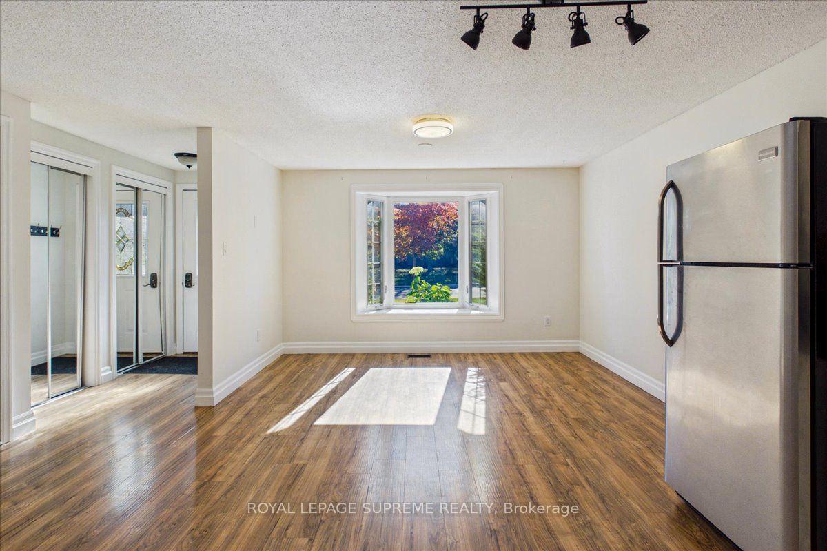 Vacant room with wood-look flooring, mirrored sliding doors, and a window overlooking autumn foliage.