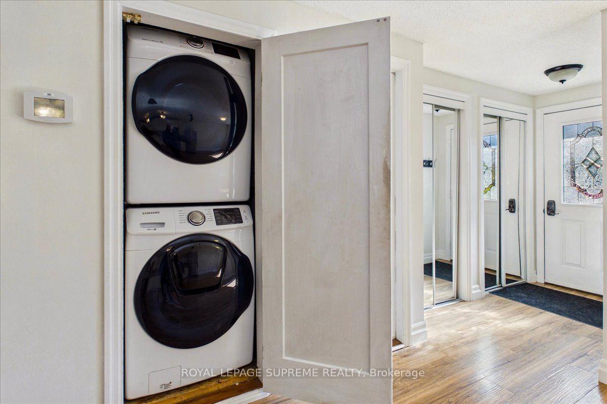 Laundry area with stacked washer and dryer beside a bright entryway with mirrored closet doors.