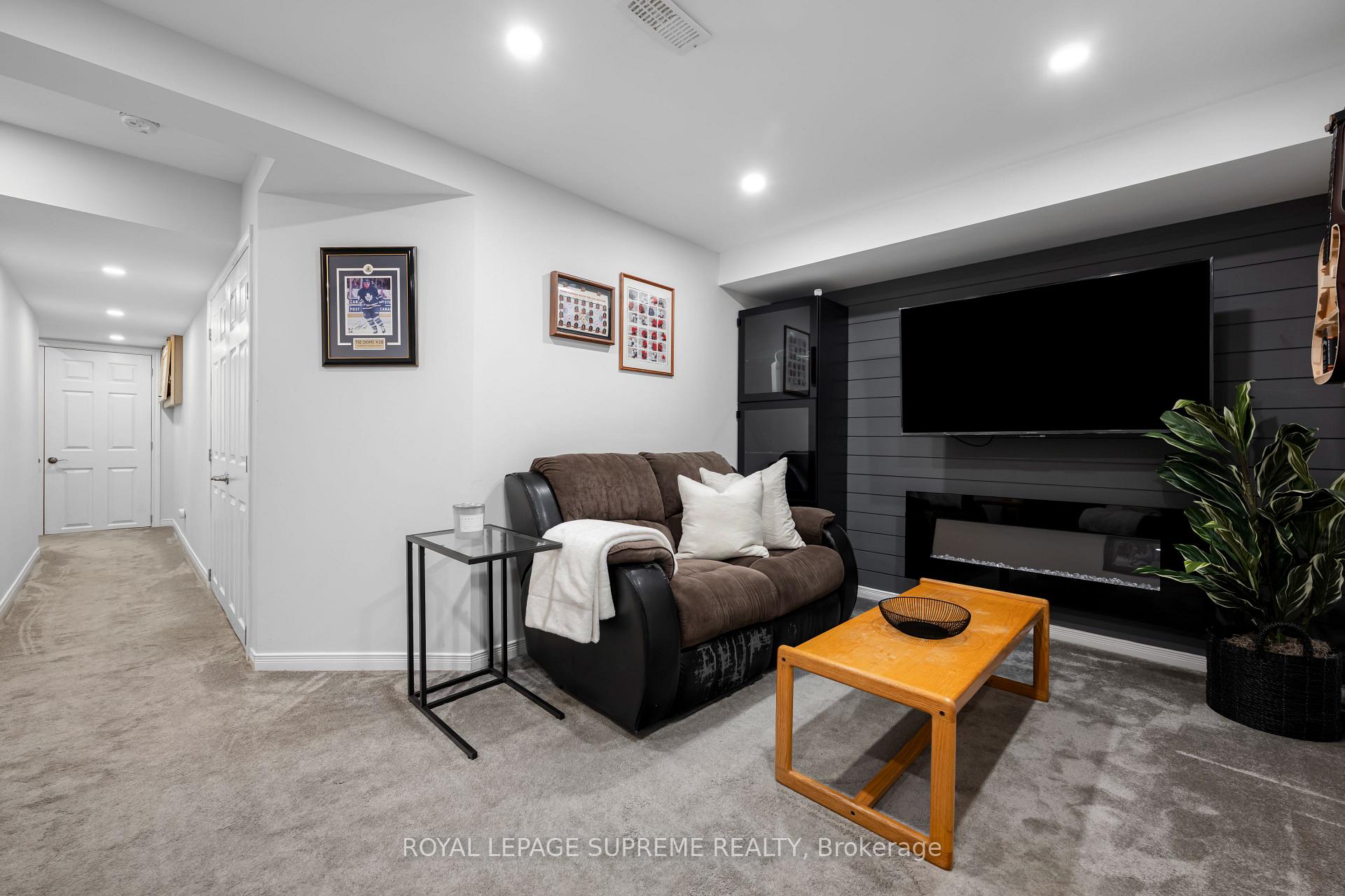 Furnished recreation room with a brown sofa, large television, black fireplace wall, and gray carpet.