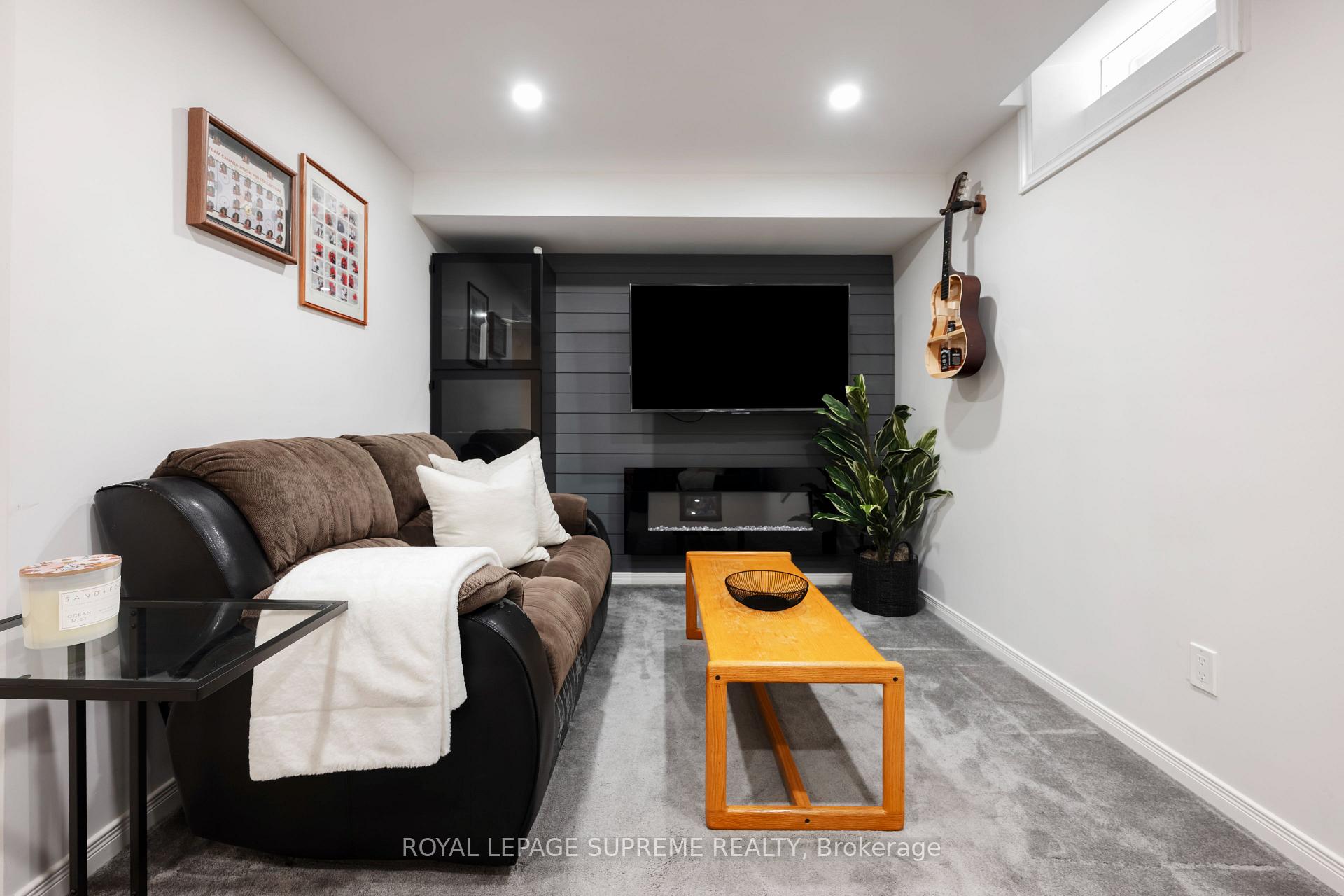 Basement family room with a brown sofa, wall-mounted TV, electric fireplace, and guitar on the wall.