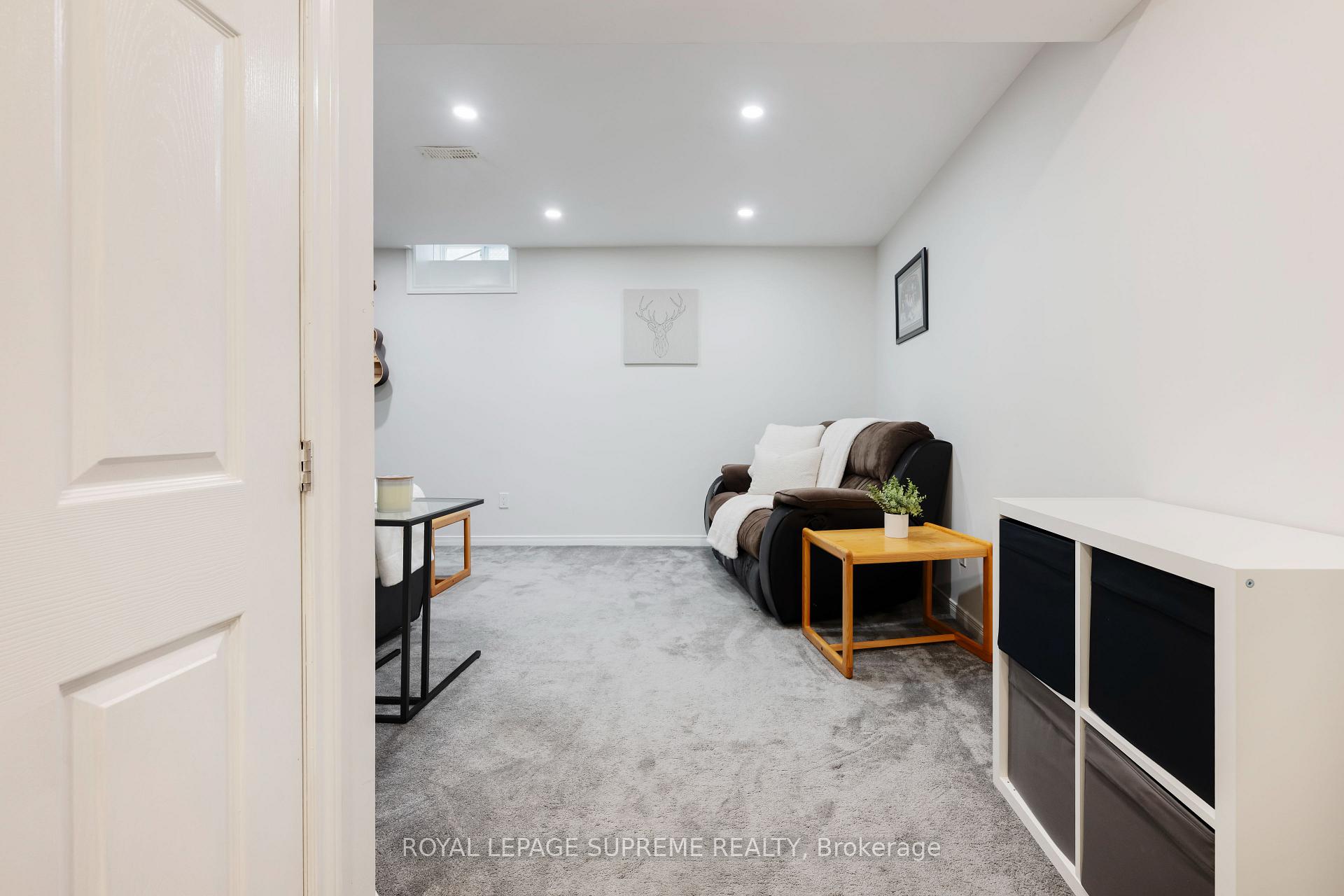 Furnished basement sitting room with gray carpet, a brown loveseat, and a wooden side table.