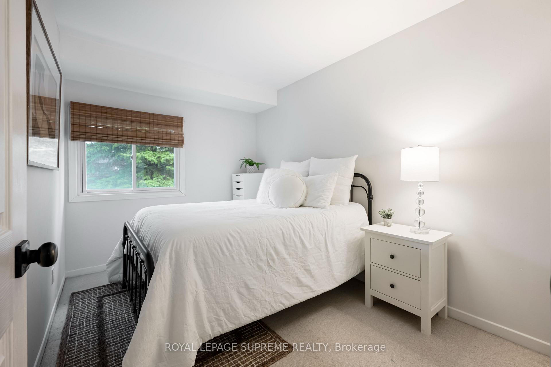 Bedroom with a black metal bed, white bedding, woven window blind, and white bedside table.