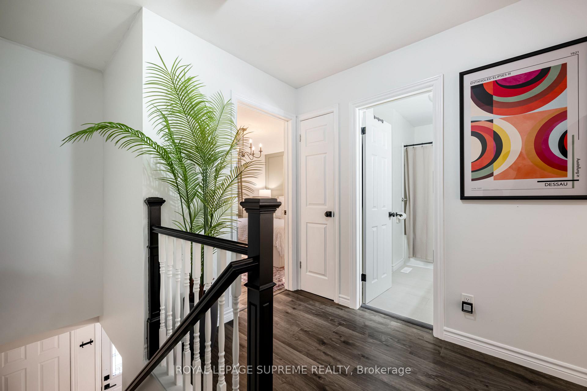 Upstairs landing with a black-and-white stair railing, tall palm, and open bathroom doorway.