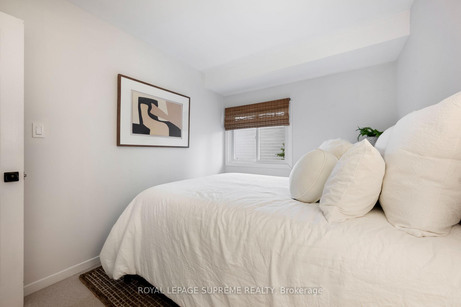 Bedroom with a white bed, framed abstract art, and a window with a woven shade.