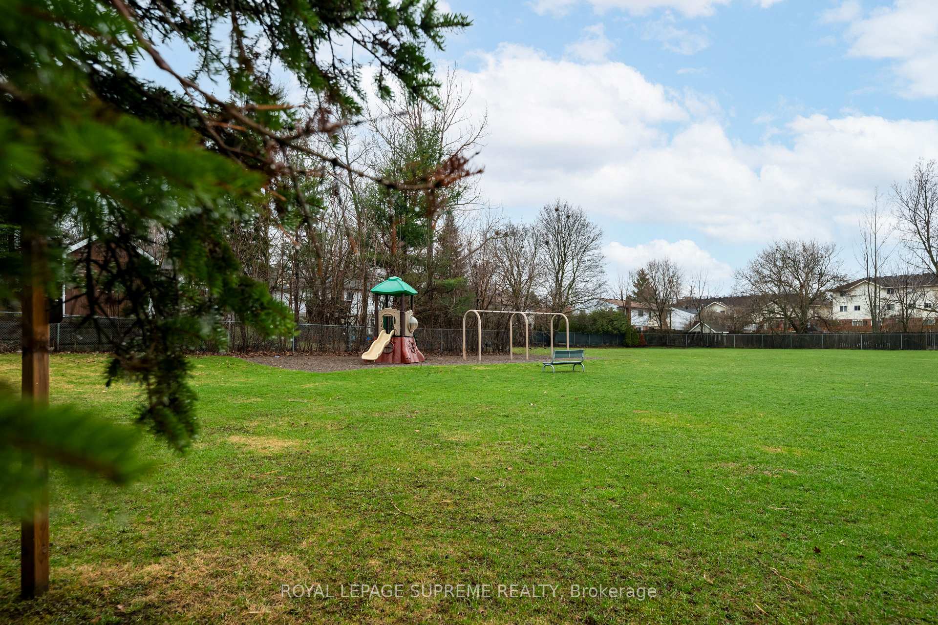 Outdoor playground with a play structure, swings and a bench on a broad grassy lawn.