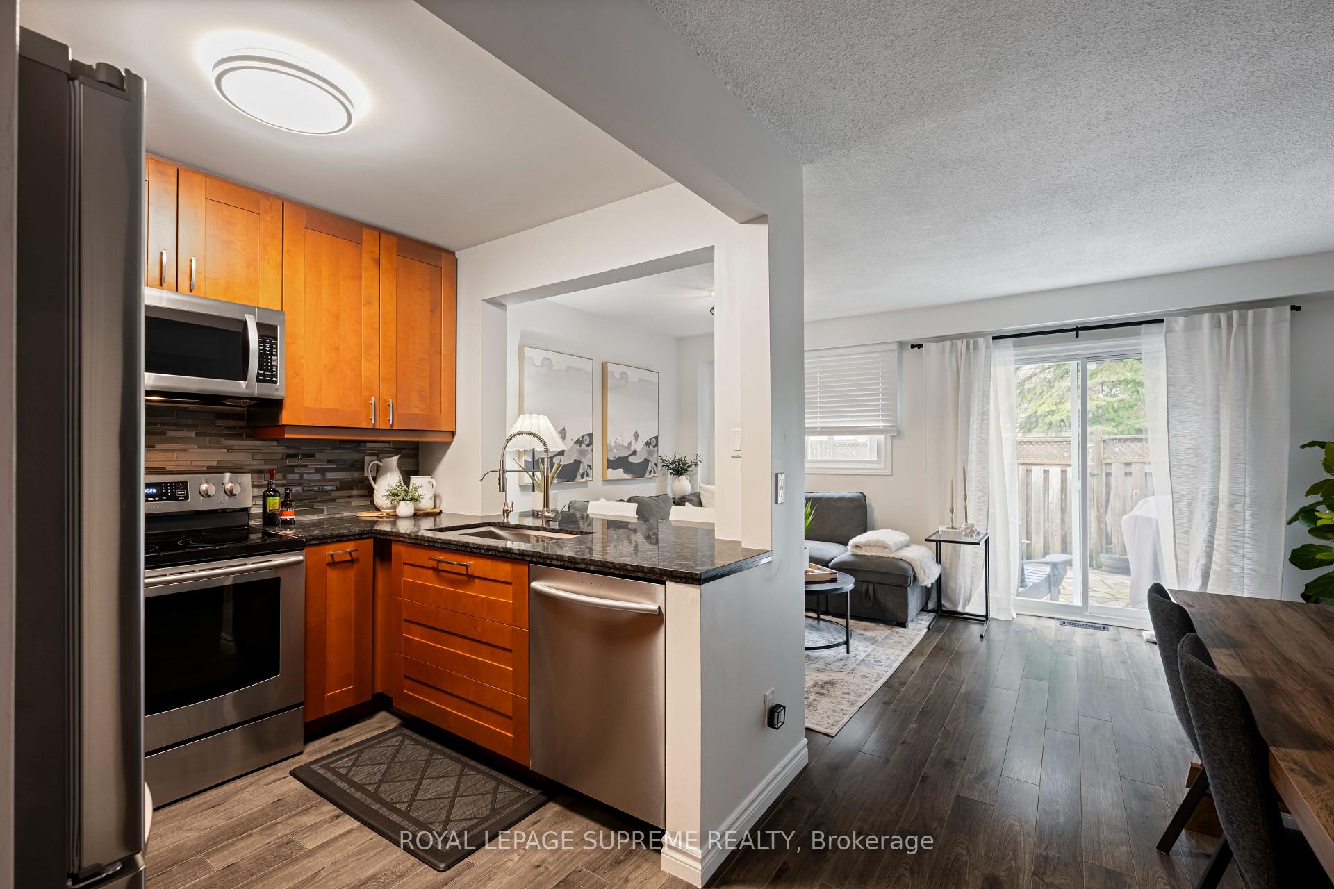 Open-concept kitchen with orange wood cabinets and stainless steel appliances, overlooking a living room with patio doors.