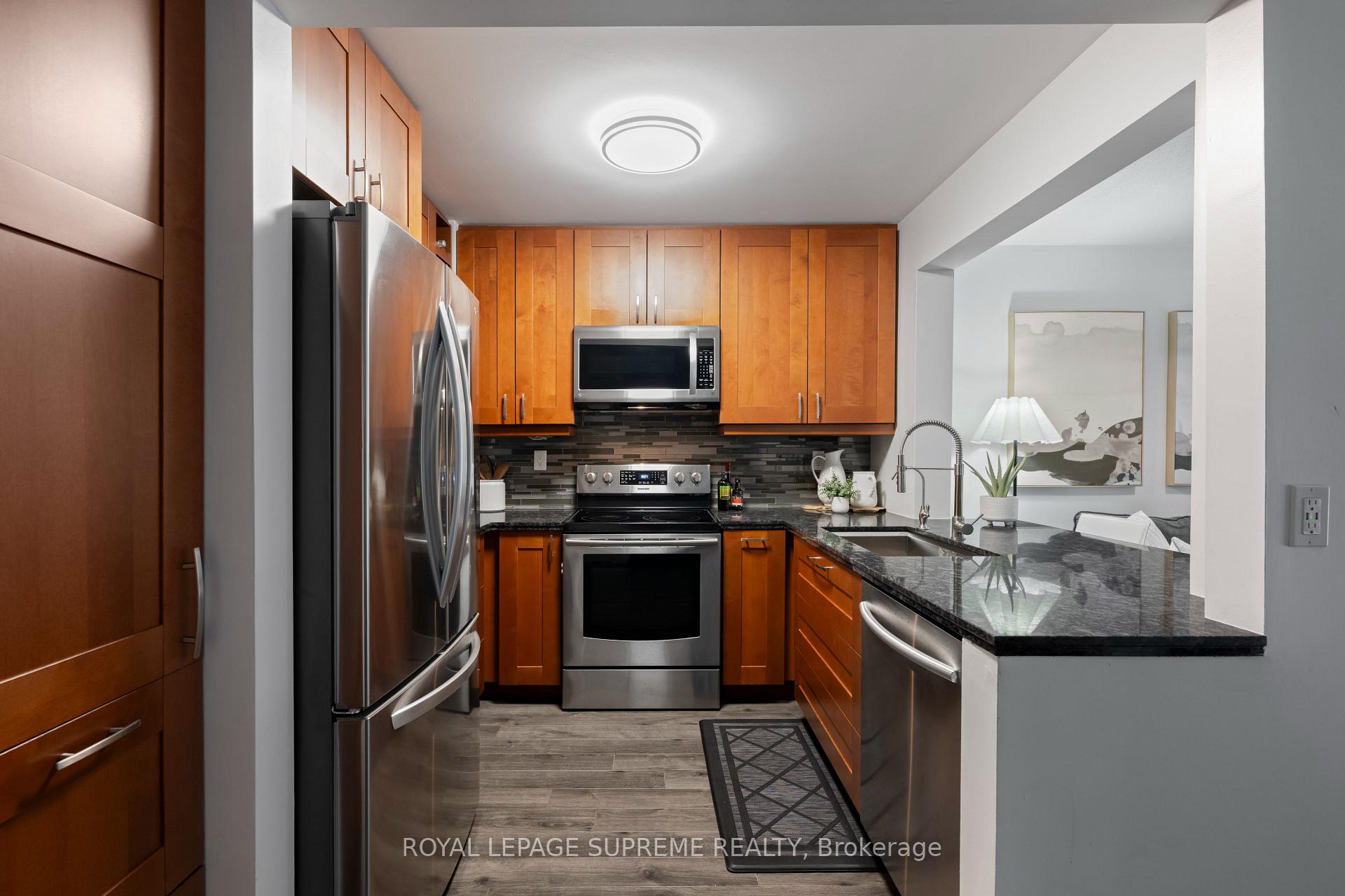 Kitchen with warm wood cabinetry, stainless steel appliances, dark counters, and a breakfast bar.