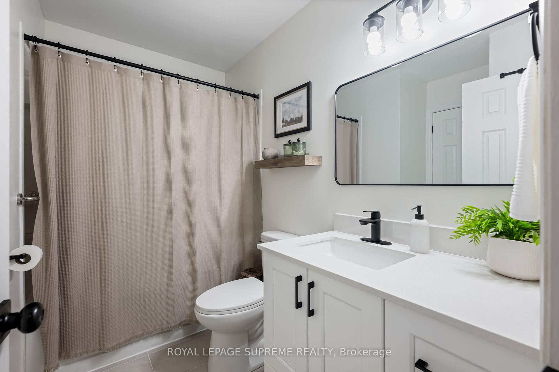 Bathroom with white vanity, black fixtures, large mirror, and beige shower curtain.