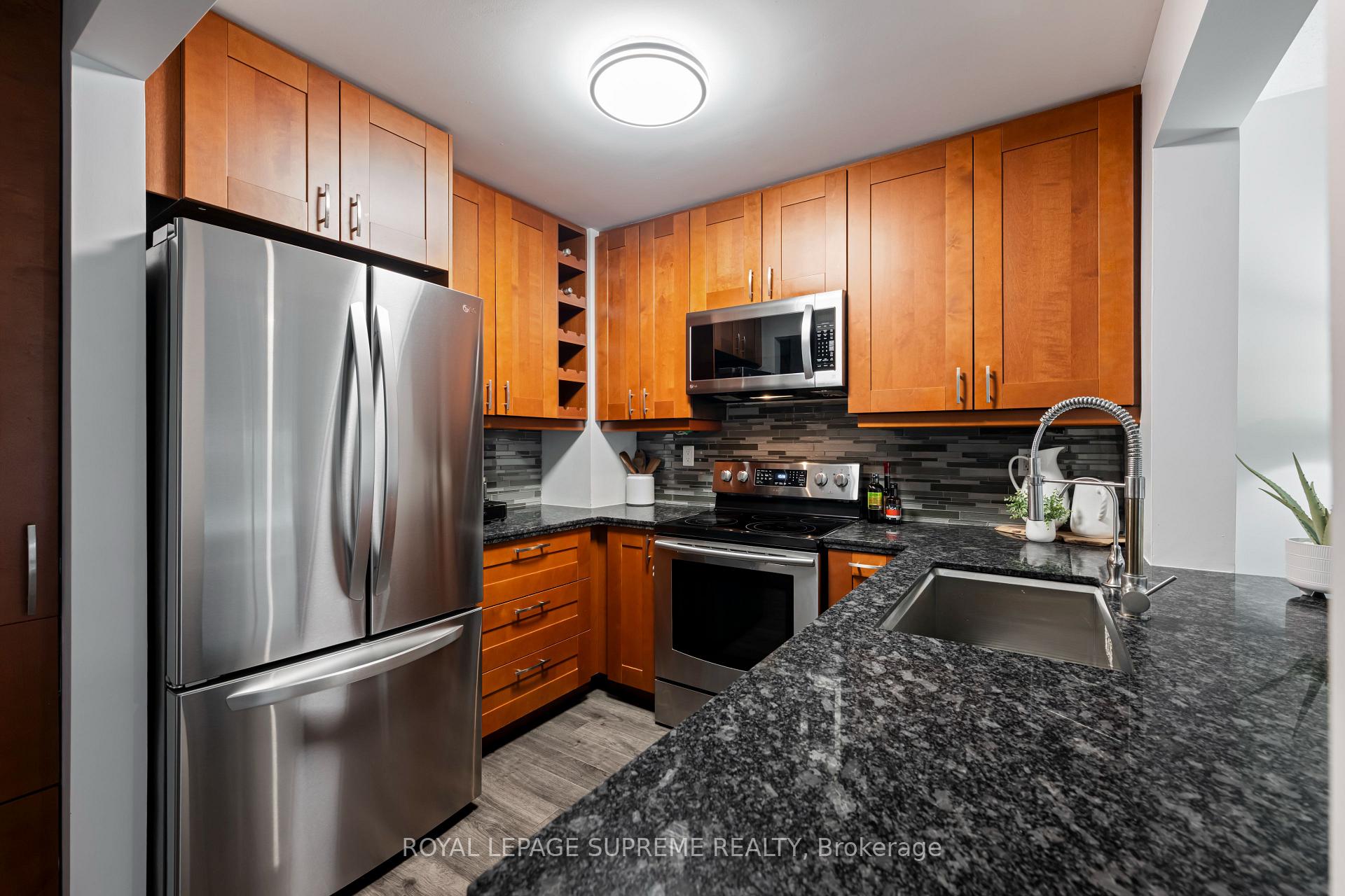 Kitchen with maple cabinets, stainless steel appliances, dark granite counters, and a gray mosaic backsplash.