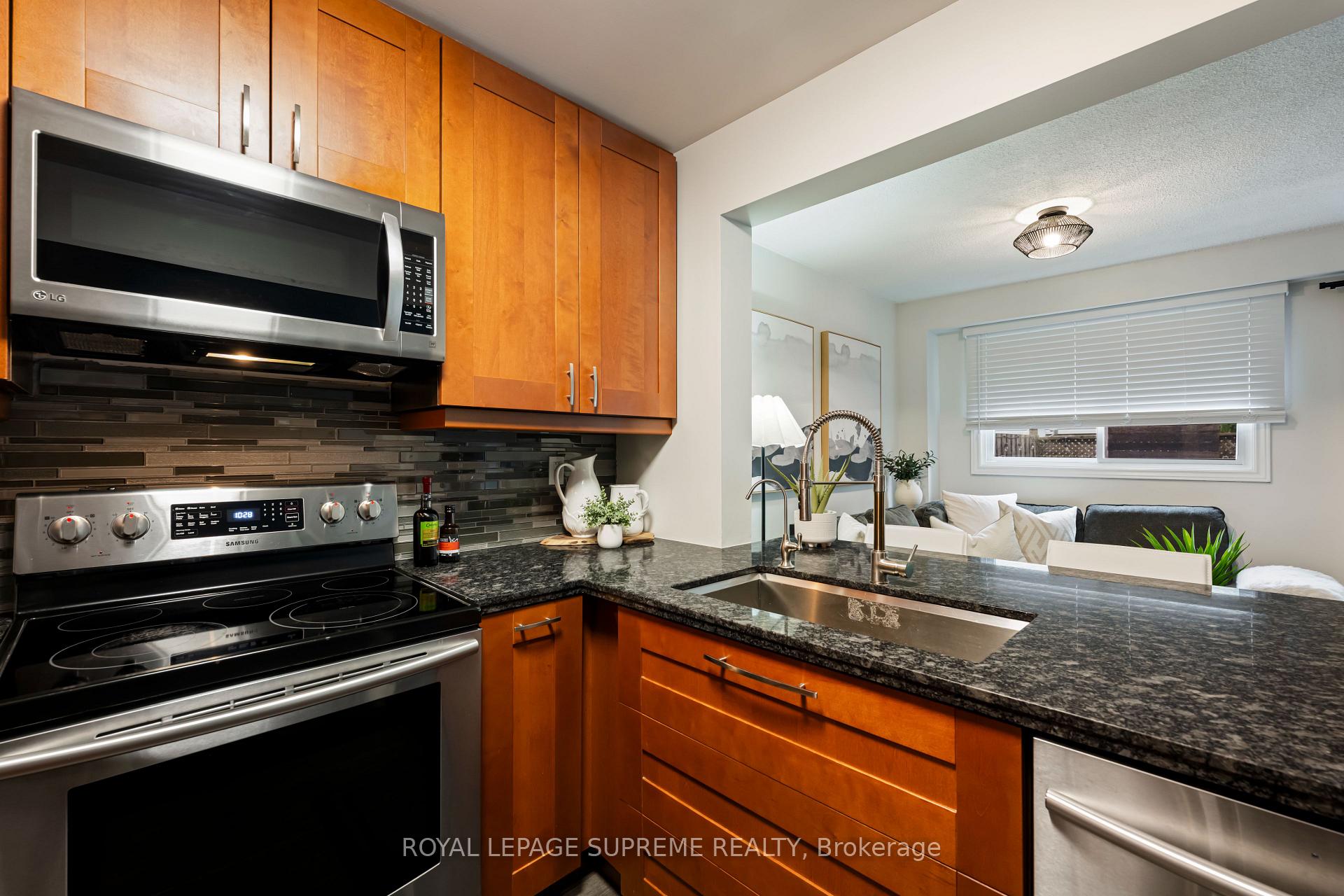 Kitchen with warm wood cabinets, dark granite counters, stainless steel appliances, and a view into the living room.