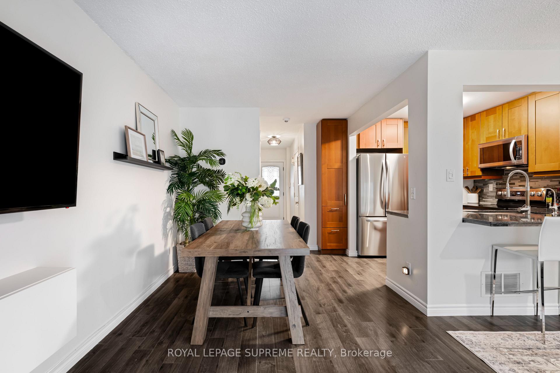 Dining area with a wood table and plants beside a kitchen with warm wood cabinets and stainless steel appliances.