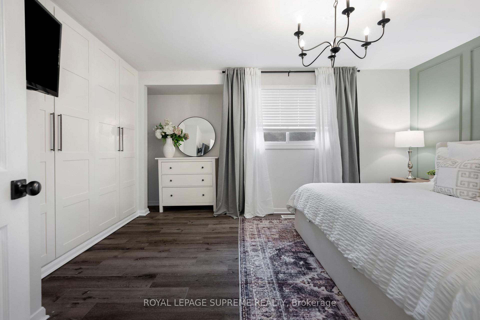 Bright bedroom with built-in white closets, gray curtains, and a dresser topped with flowers and a round mirror.