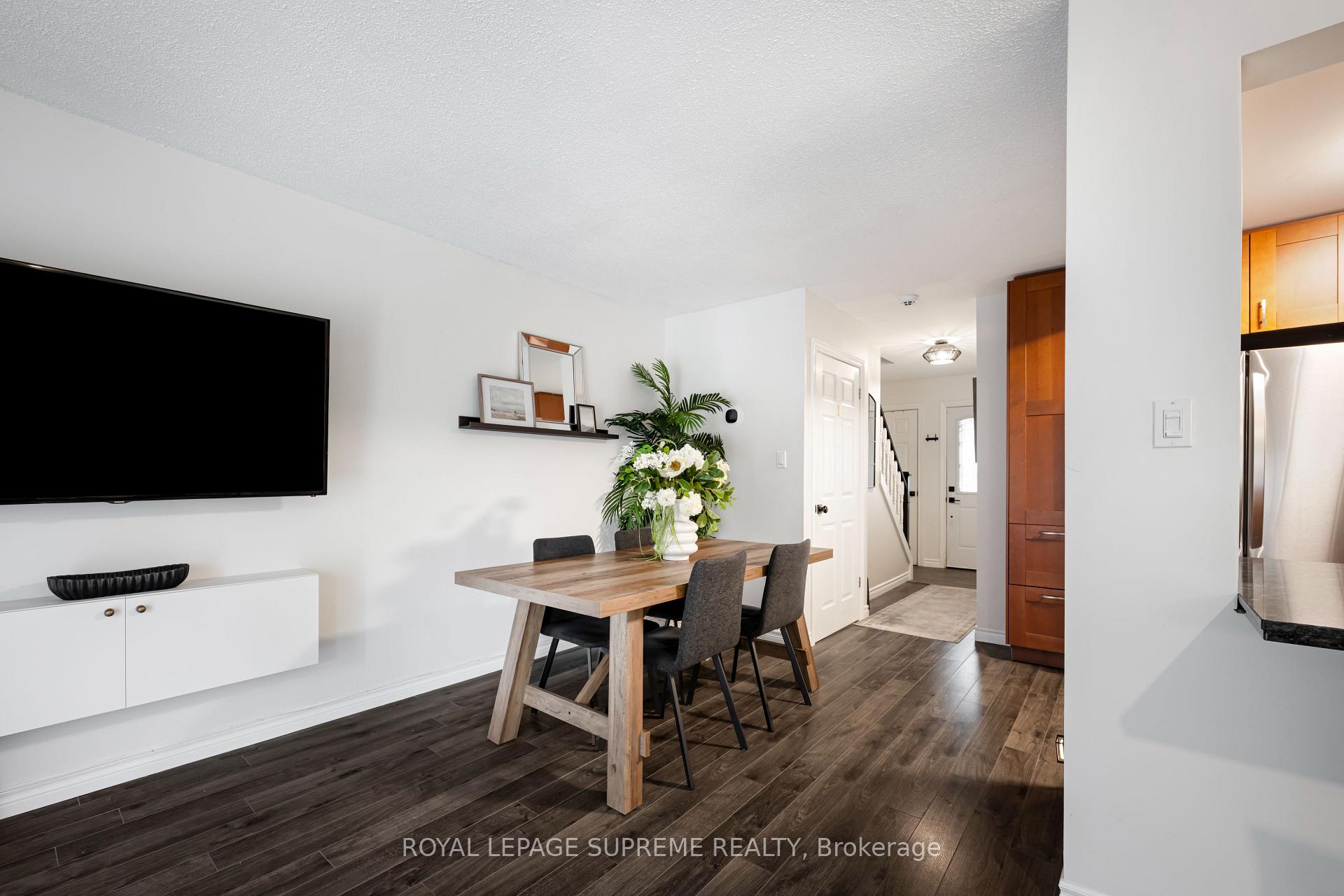 Dining area with a wood table and gray chairs beside the living room television and entry hall.