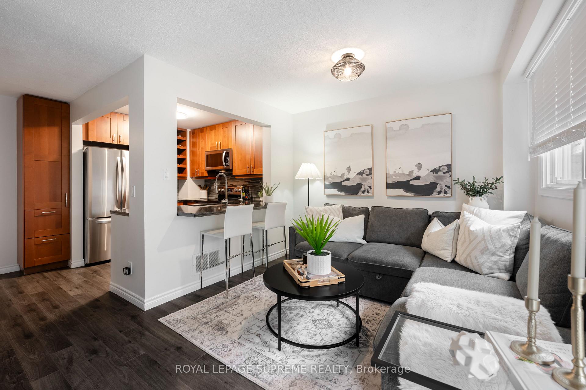 Open-plan living room and kitchen with a gray sectional, warm wood cabinets, and a breakfast bar.