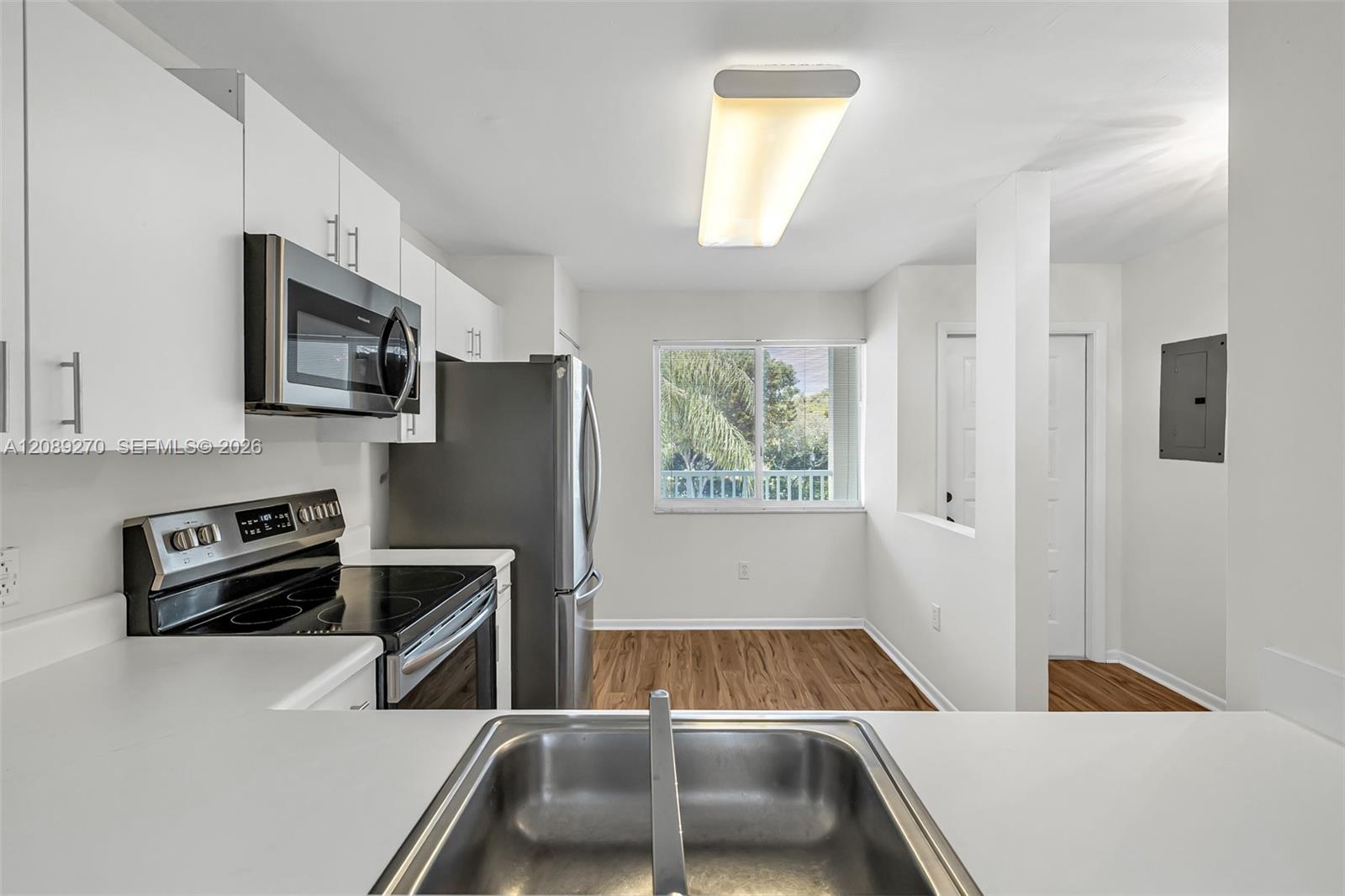 Vacant condo kitchen with white cabinets, stainless-steel appliances, and wood-look flooring.