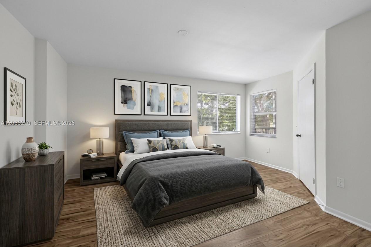 Staged bedroom with a dark upholstered bed, gray bedding, and two bright windows.