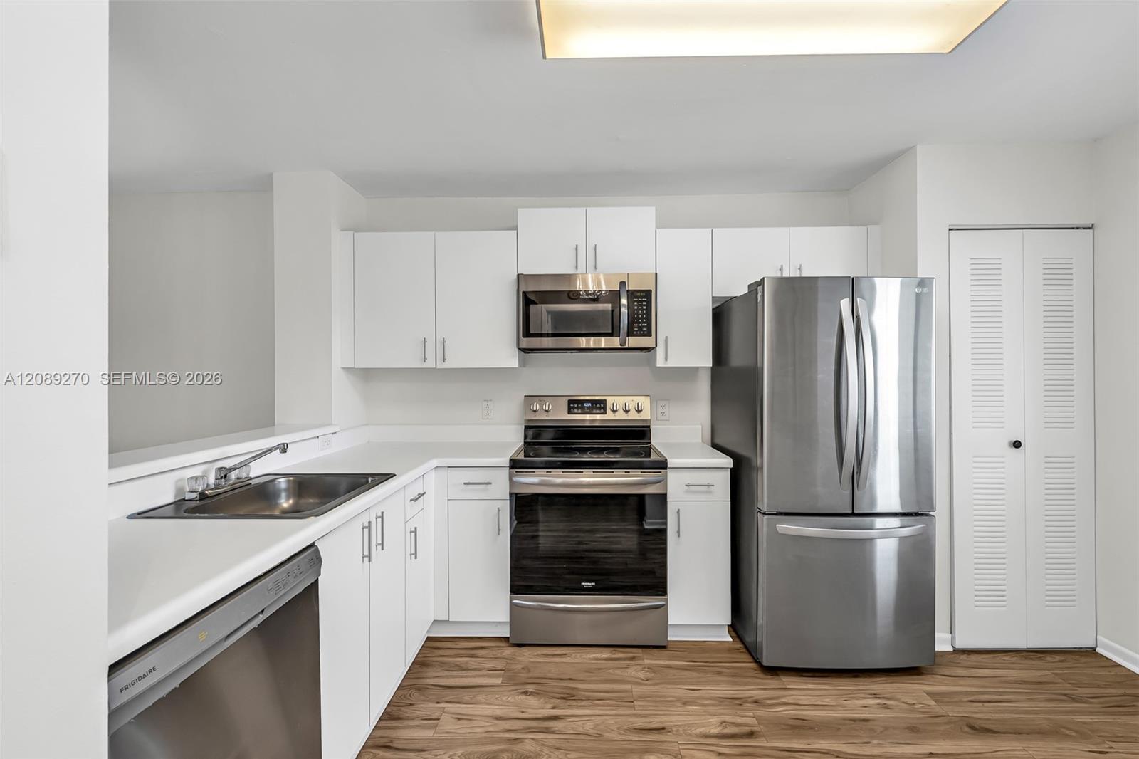Unfurnished kitchen with white cabinets, stainless steel appliances, and wood-look flooring.
