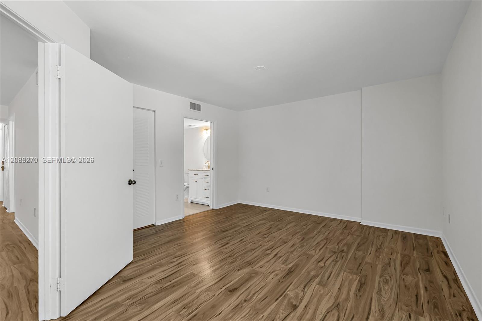 Empty room with wood-look flooring and an open doorway to a bathroom vanity.