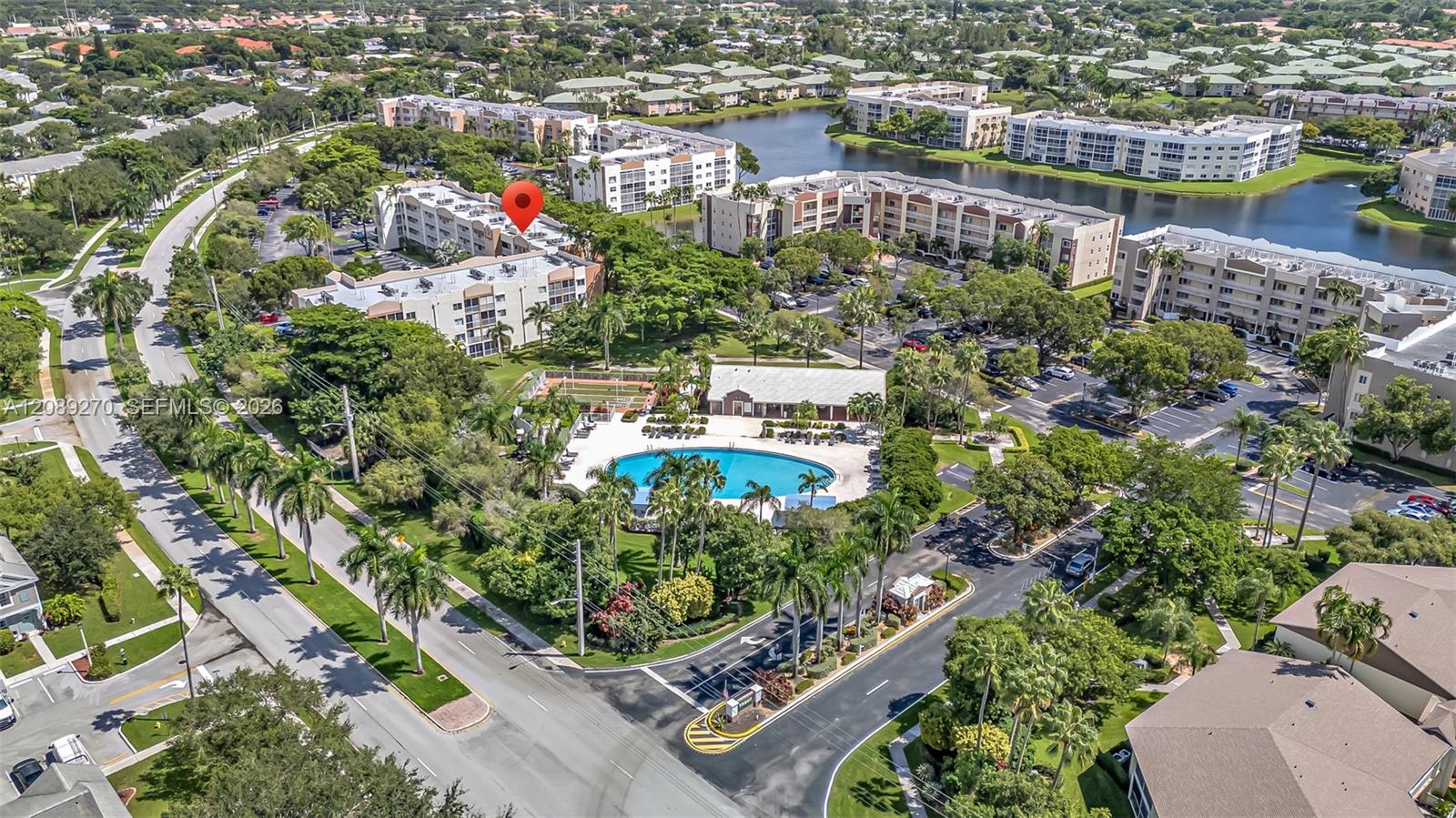 Aerial view of condo buildings beside a lake, with a red location pin and community pool.