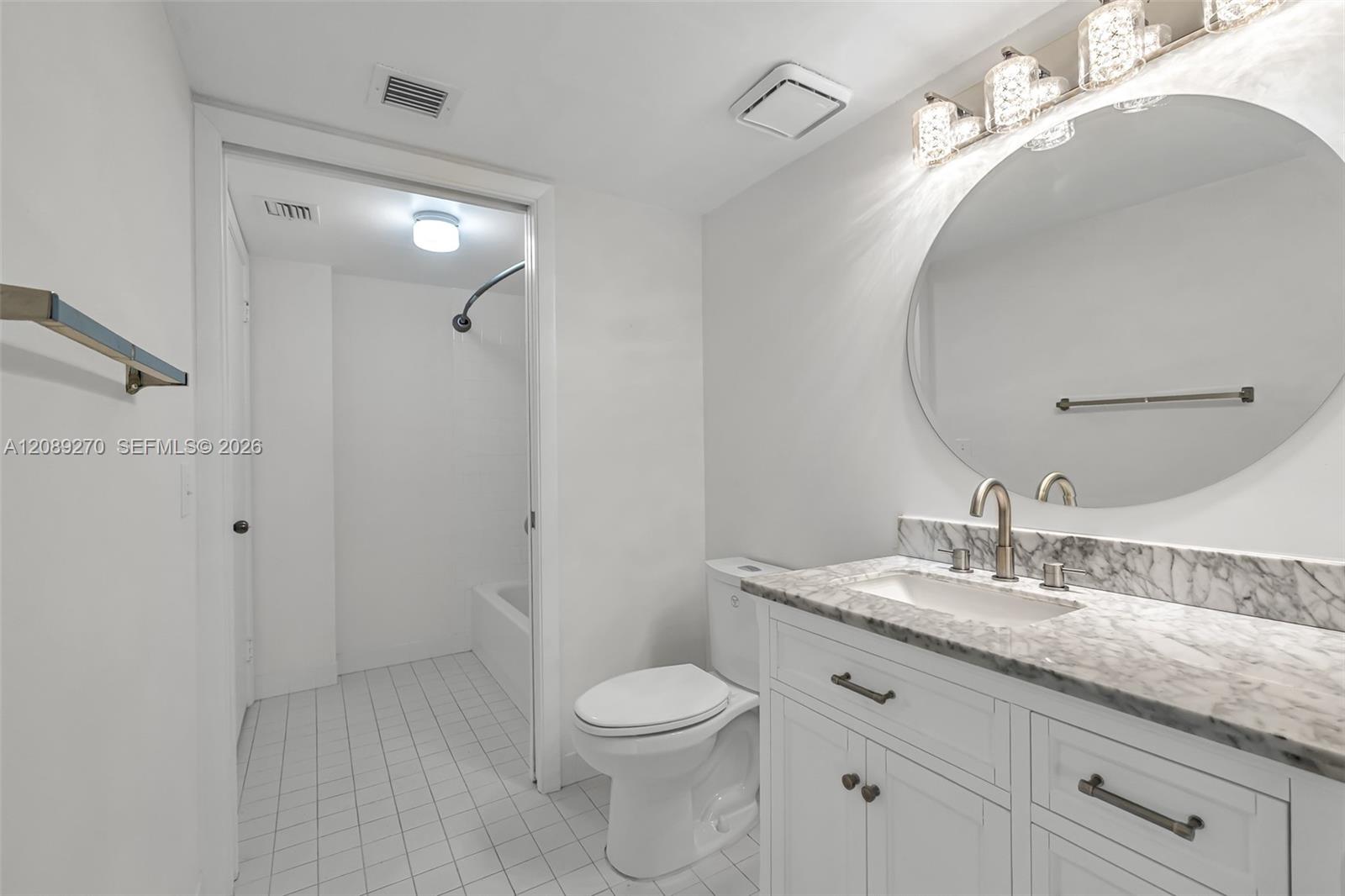 Bright white bathroom with marble vanity, oval mirror, and tub-shower.
