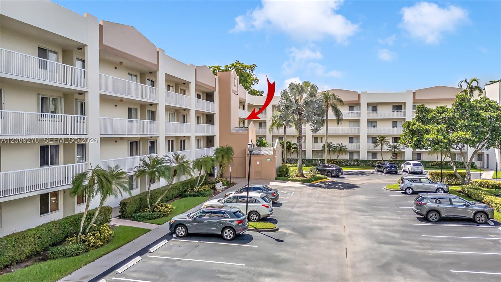 Condominium complex with white balconies and palm trees; a red arrow points toward a unit.