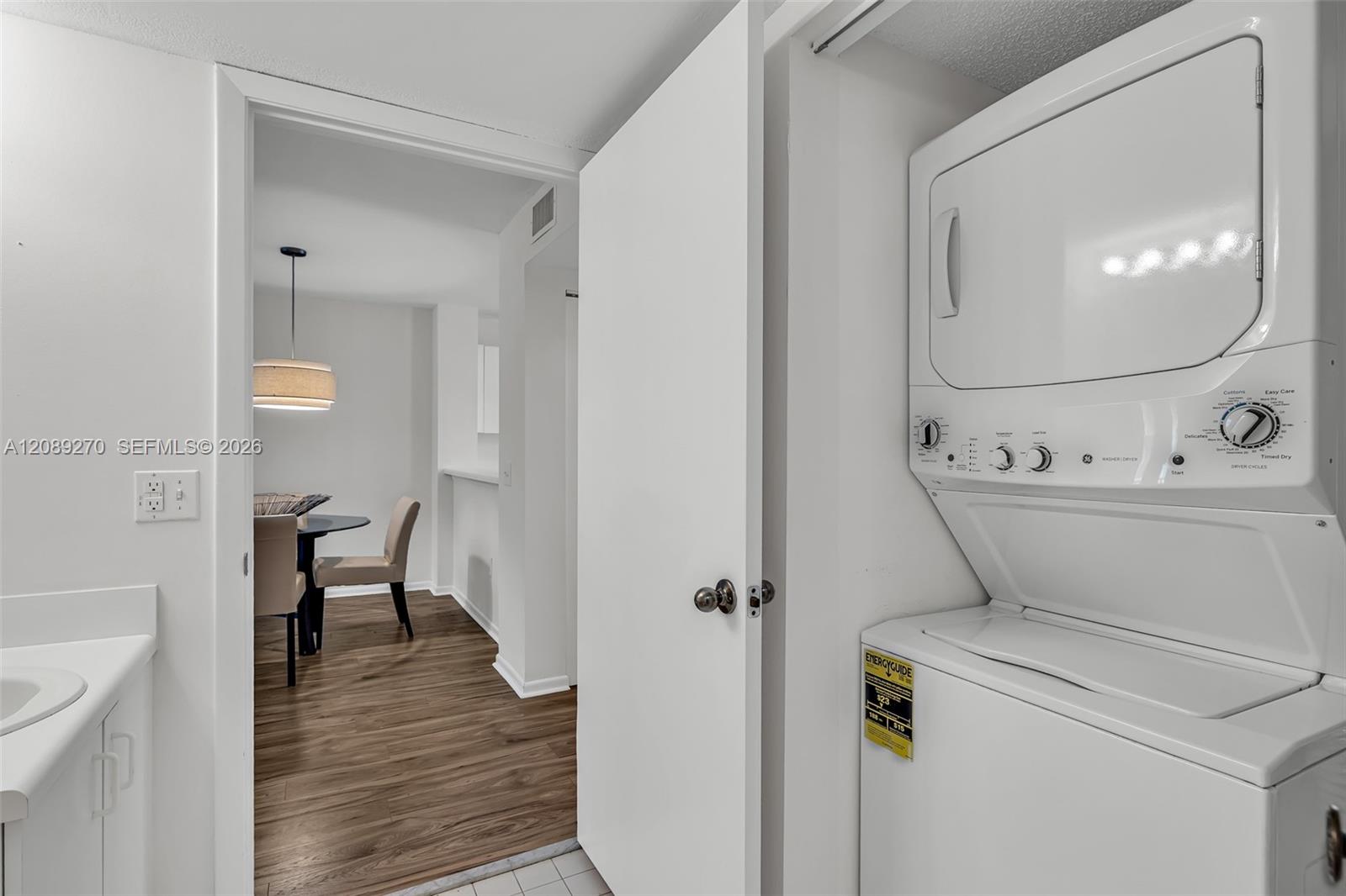 Laundry area with a stacked washer and dryer beside an open doorway to a dining nook.