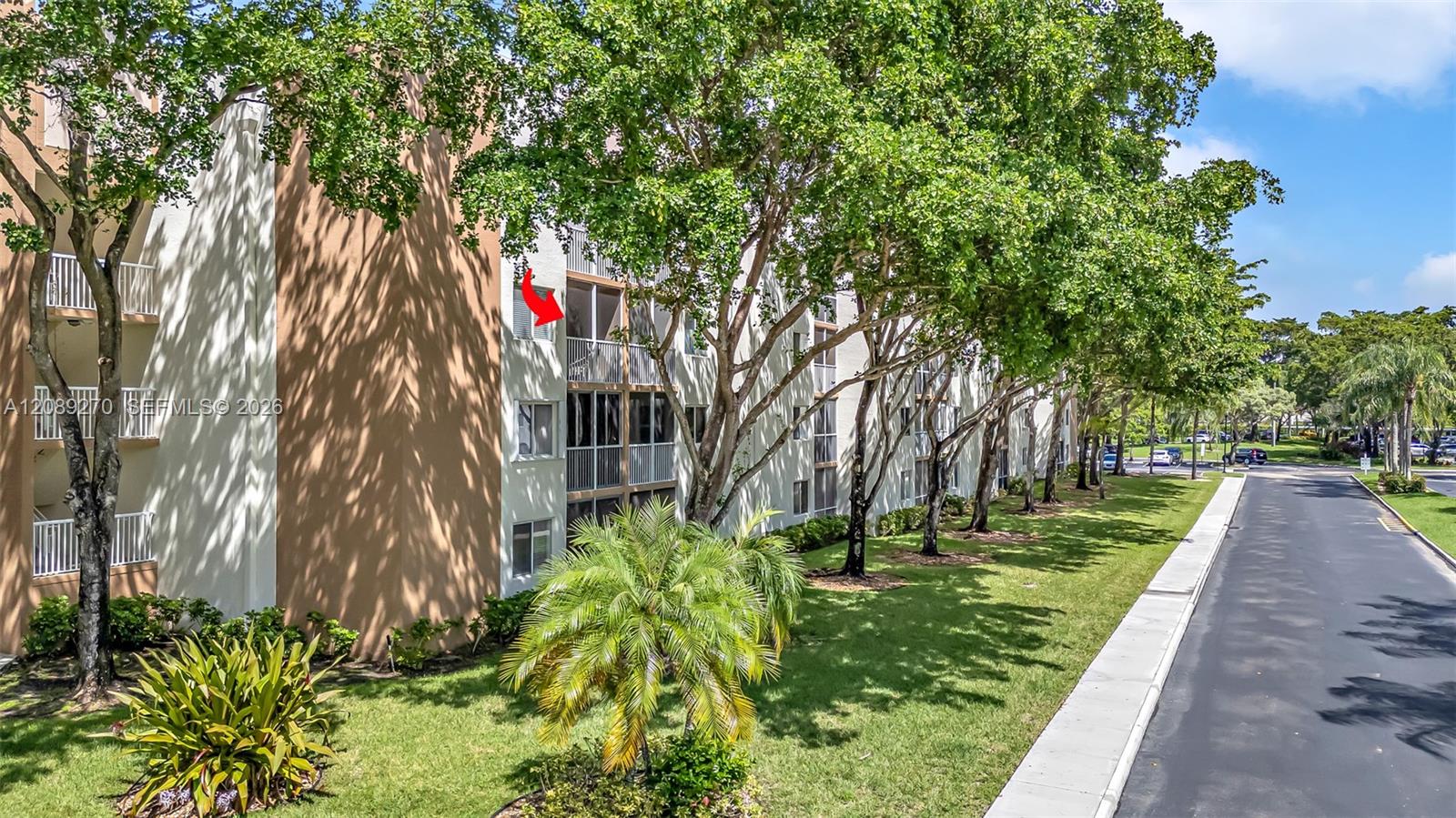 Condominium exterior with a red arrow marking an upper-floor balcony beside a tree-lined drive.