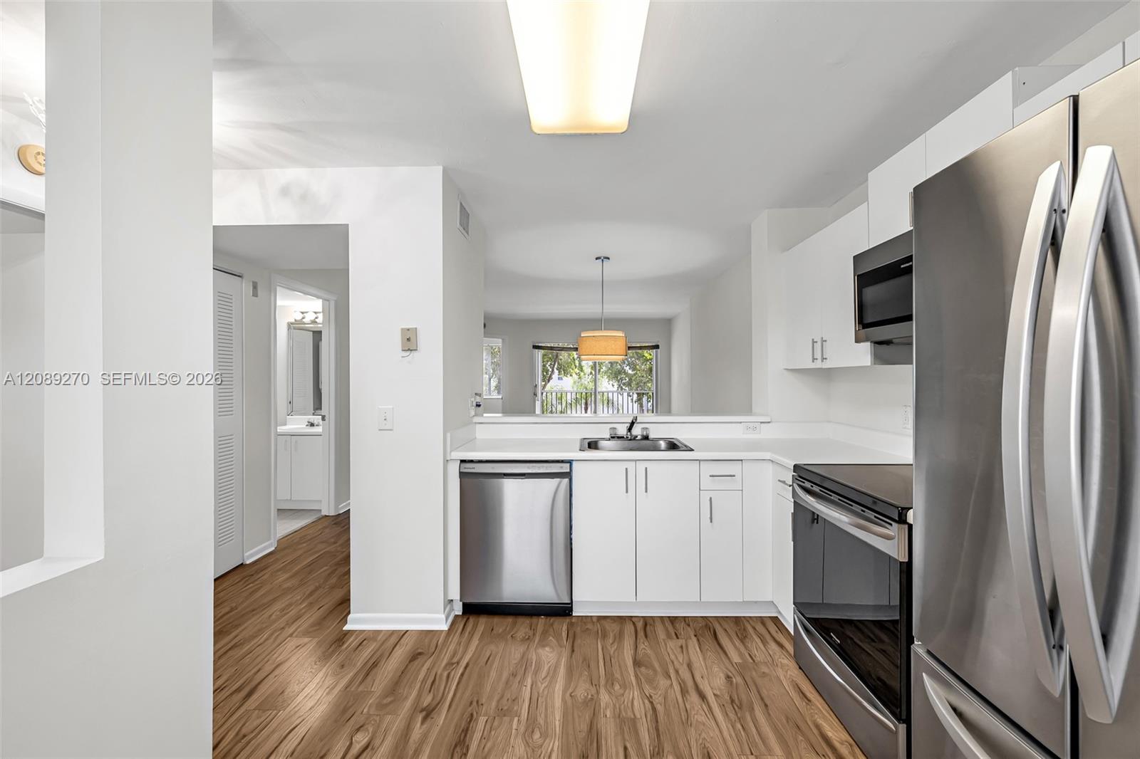Bright white kitchen with stainless steel appliances, wood-look floors, and a view toward the balcony.